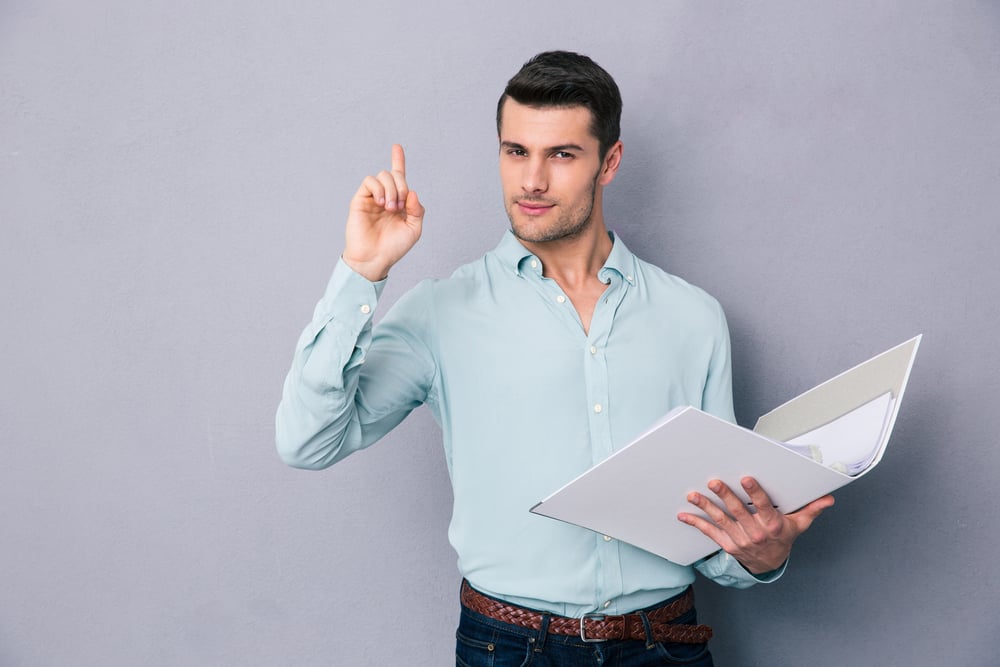 Handsome man holding folder and pointing finger up over gray background. Having idea!