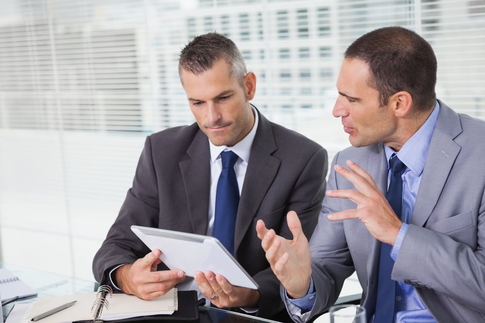 Serious businessmen analyzing documents on their tablet in bright office