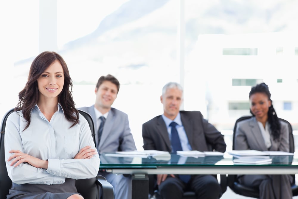 Smiling businesswoman sitting and crossing her arms while accompanied by her team