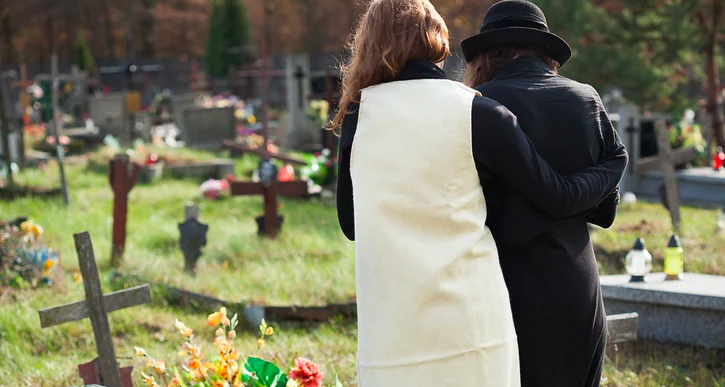 Twee vrouwen op begraafplaats, rugaanzicht, de een troost de ander.