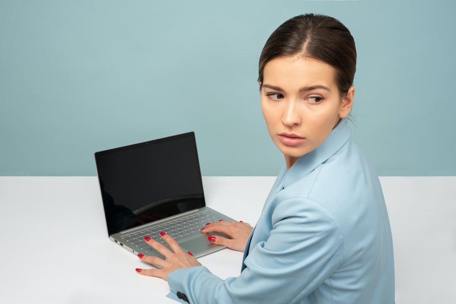 Vrouw zit voor laptop en kijkt zorgelijk over schouder heen