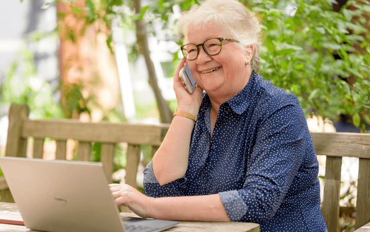 Vrouw zit voor laptop en is aan de telefoon.