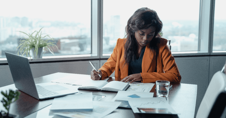 Vrouw zit aan bureau en bekijkt haar administratie op tafel