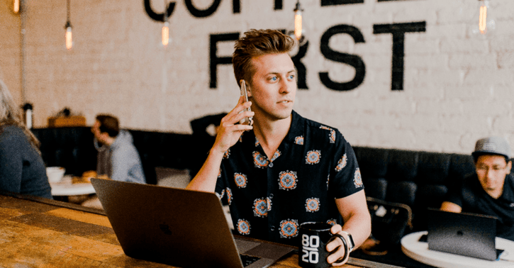 Man zit in een cafe met zijn laptop en hij is aan de telefoon