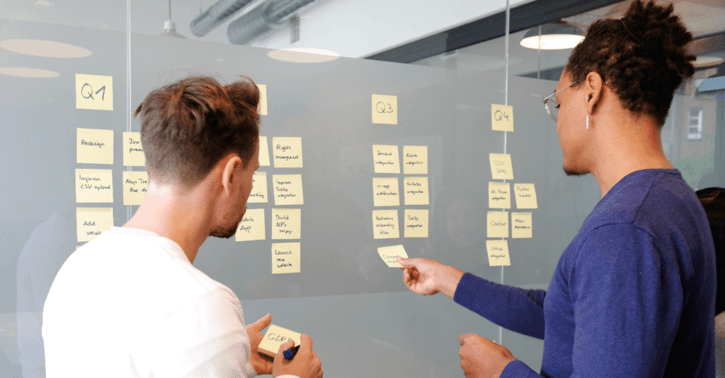 Collega's plakken plakbriefjes op glazen wand