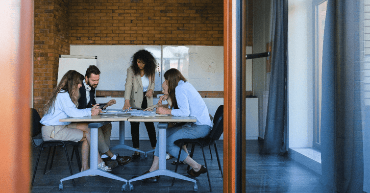 Collega's staan om een tafel heen en overleggen