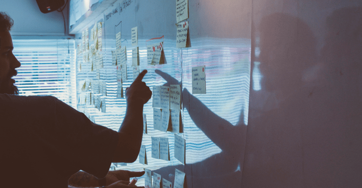 Persoon wijst naar whiteboards waar plaknotities op geplakt zijn