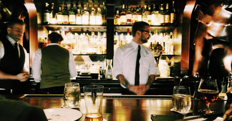Man staat achter bar, terwijl ander personeel om hem heen beweegt.