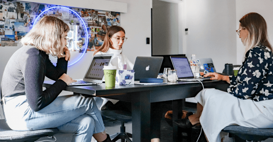 Drie collega's zitten om een tafel heen voor hun laptop