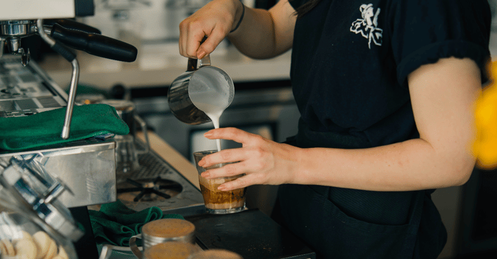 Persoon staat achter een bar en schenkt koffie in
