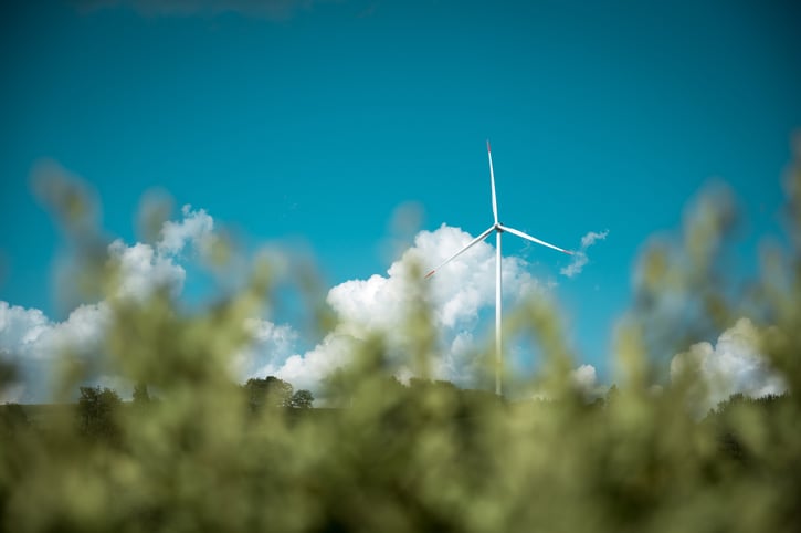 Een foto van een windturbine tegen een felblauwe lucht met witte wolken