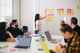 Vrouw geeft presentatie aan collega's en wijst naar post its op de muur.