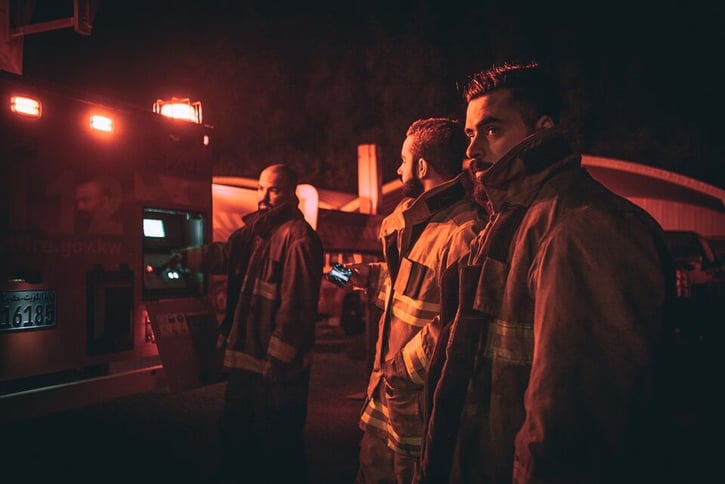 Brandweermannen staan te wachten bij de auto, het is nacht.