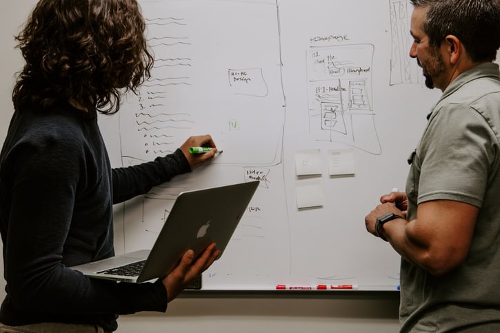 Twee mensen staan te overleggen voor een whiteboard