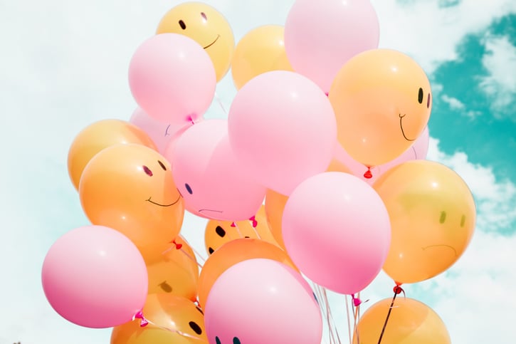 Gele en roze ballonnen met smiley gezichtjes met een wolken achtergrond