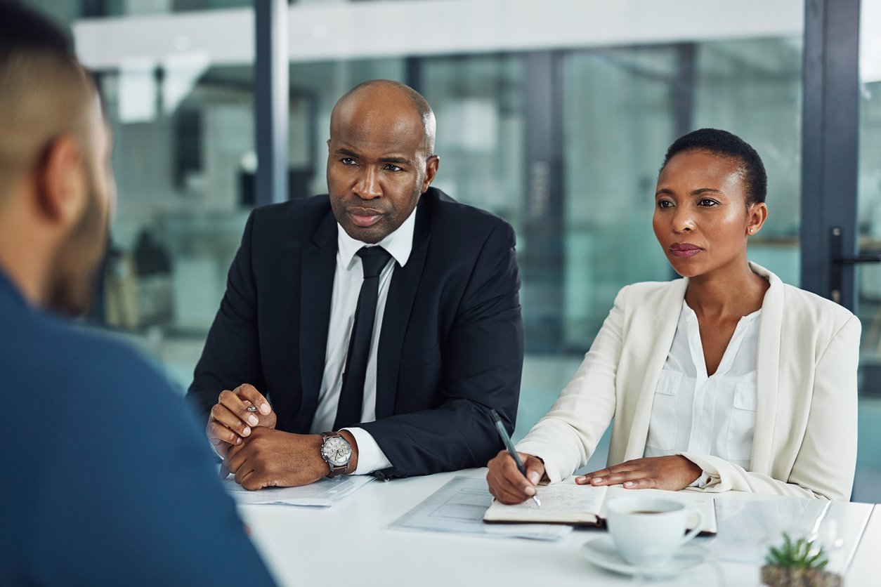 male and female African-American executives interviewing a male black applicant using cultural fit interview questions while sitting inside an office