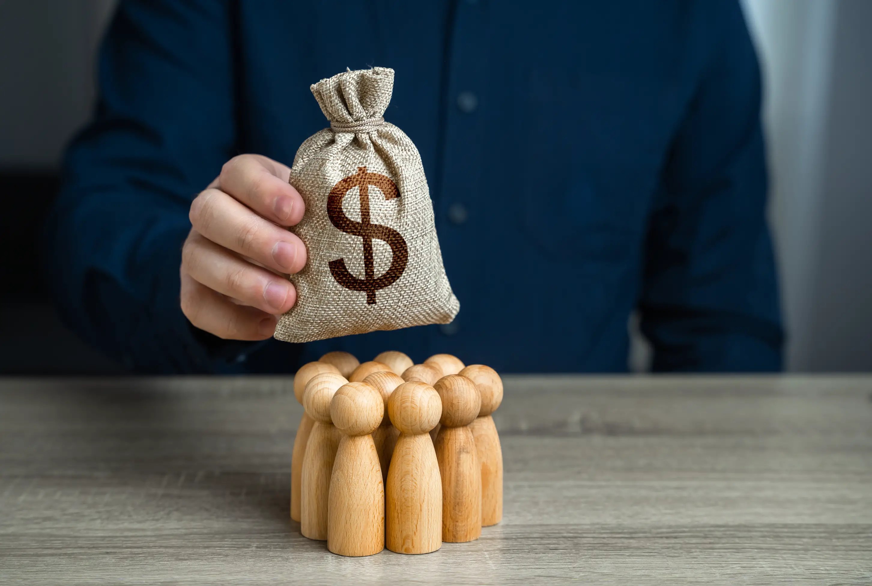 man holding money bag with dollar sign on top of wooden blocks symbolizing employee salary pay or bonus pay