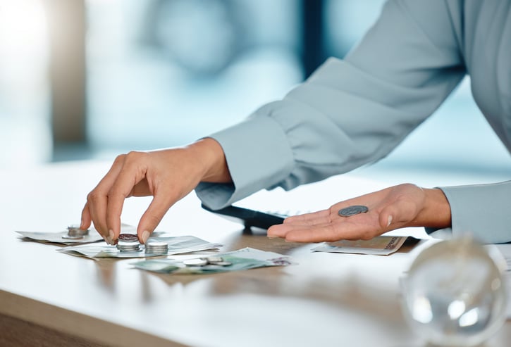 hand on table counting dollar bills and coins symbolizing paying employees in arrears