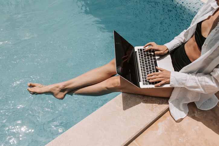 Vrouw zit aan de rand van een zwembad met laptop op schoot