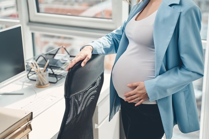 pregnant employee standing next to office chair illustrating maternity leave
