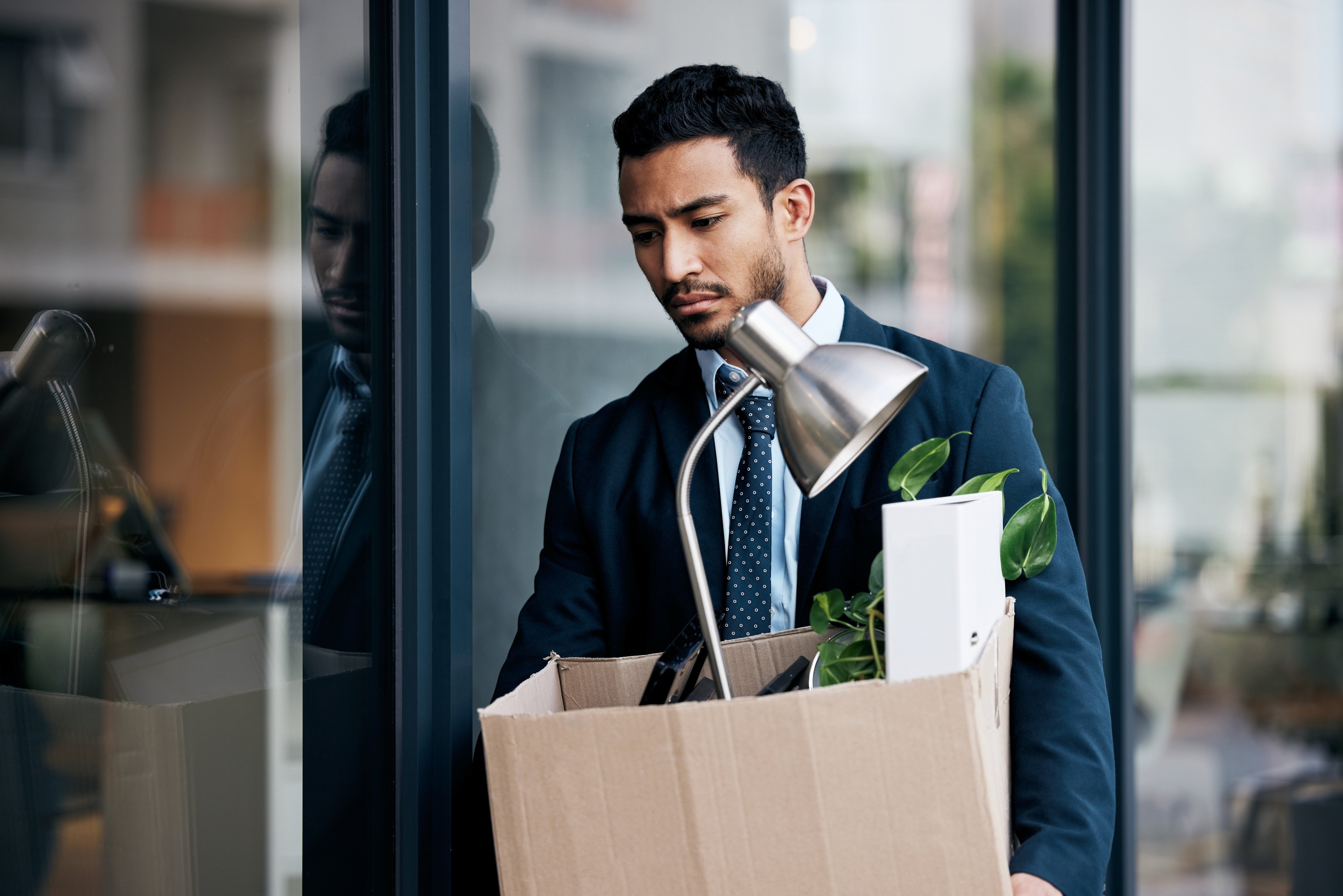 sad and fired employee leaving workplace with box of belongings in hand