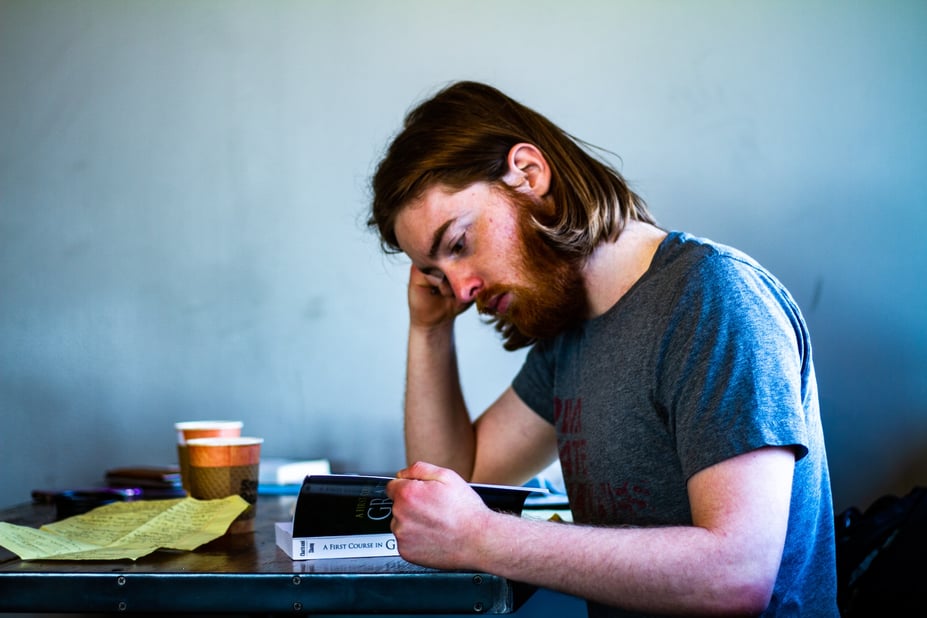 Zijaanzicht van man die aan tafel zit en een boek leest.