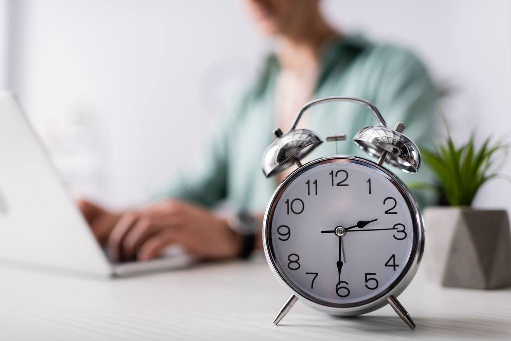 selective focus of alarm clock on table near man using laptop