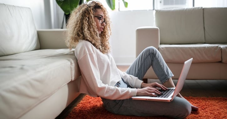 Vrouw zit tegen haar bank aan op de grond, met laptop op schoot