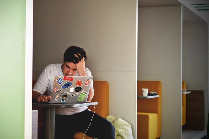 Man zit op een bankje, heeft zijn laptop voor zich en lijkt gestresst.