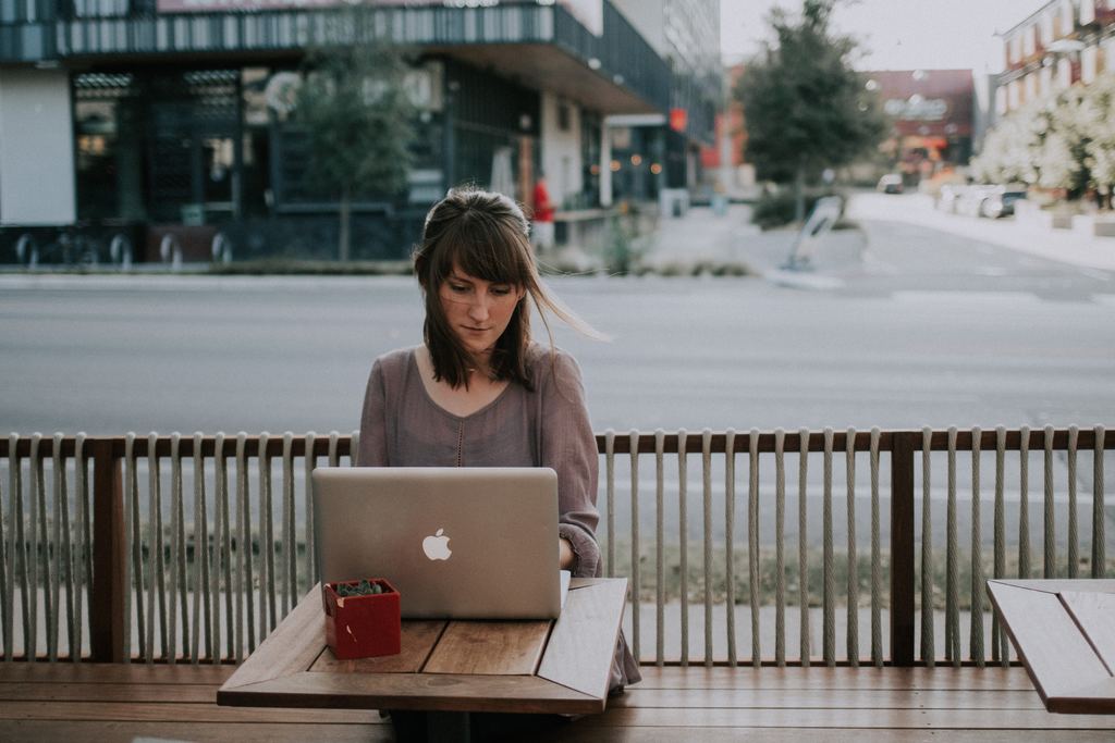 women sitting outdoors on a bench working on laptop