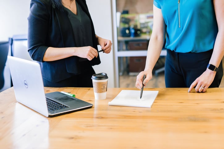 Vrouwen staan buij een bureau en zijn aan het overleggen