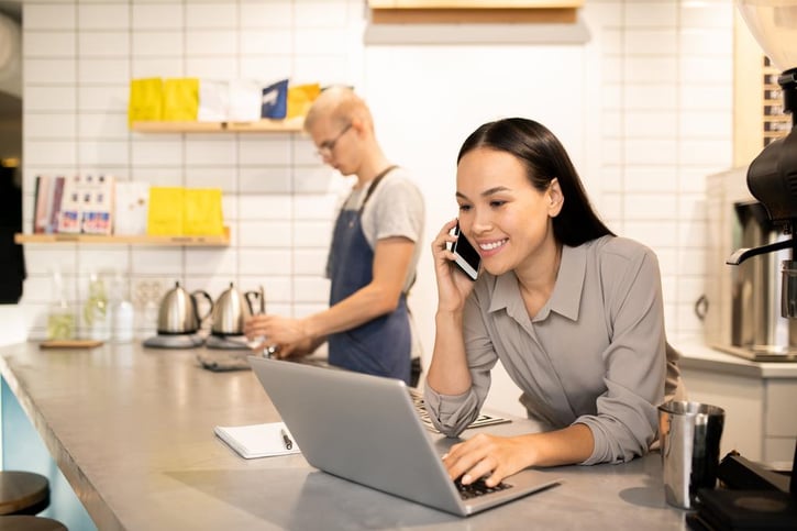 young manager of restaurant working on laptop while talking with clients on the phone